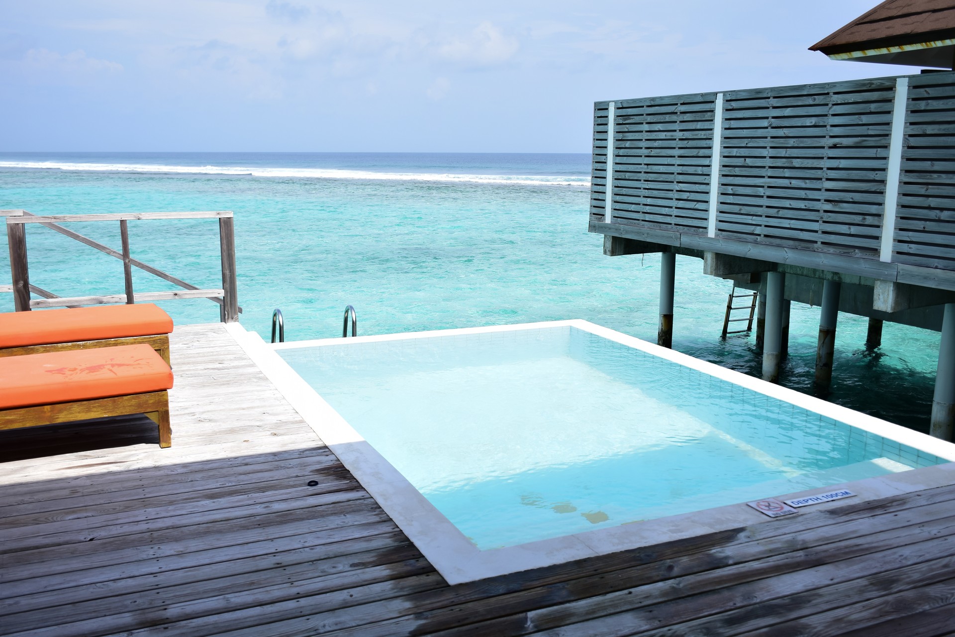 Maldives island landscape. Water, sand and greenery. Lush, tropical, vegetation, palm trees and bushes Shoreline with sandy beach. Wooden pathway pier. Walkway deck to private villas. Floating house