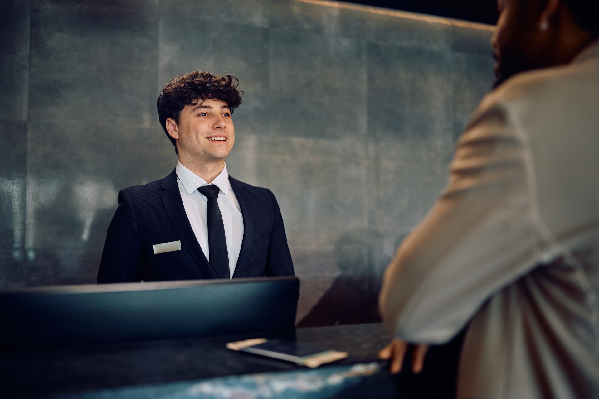 Happy receptionist serving a guest at hotel front desk.